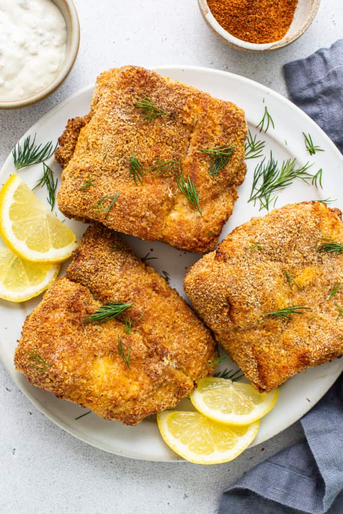 Air fryer fish on a plate with lemon slices.