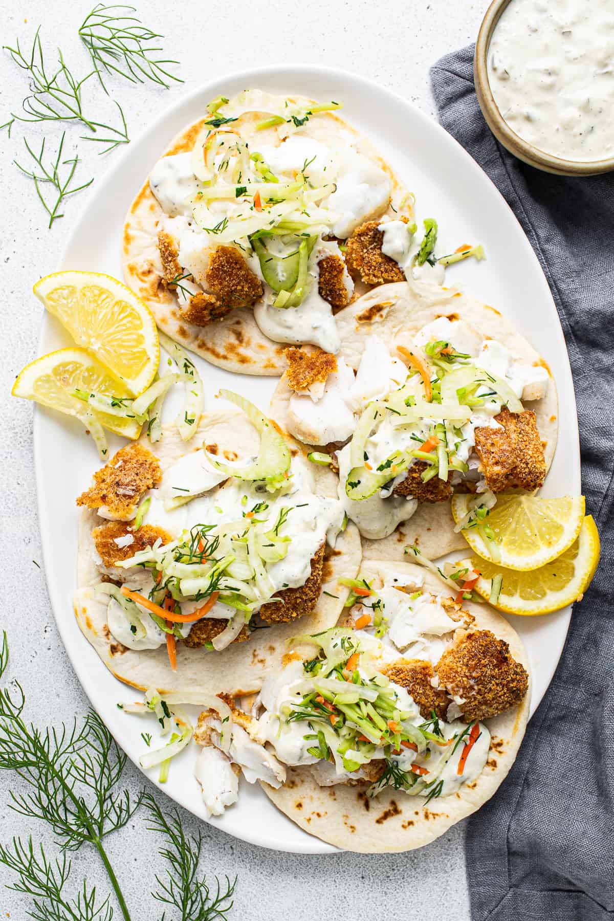 Fish tacos on a white plate with lemon wedges.