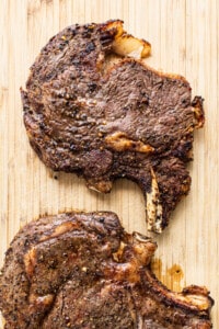 Two steaks on a wooden cutting board.