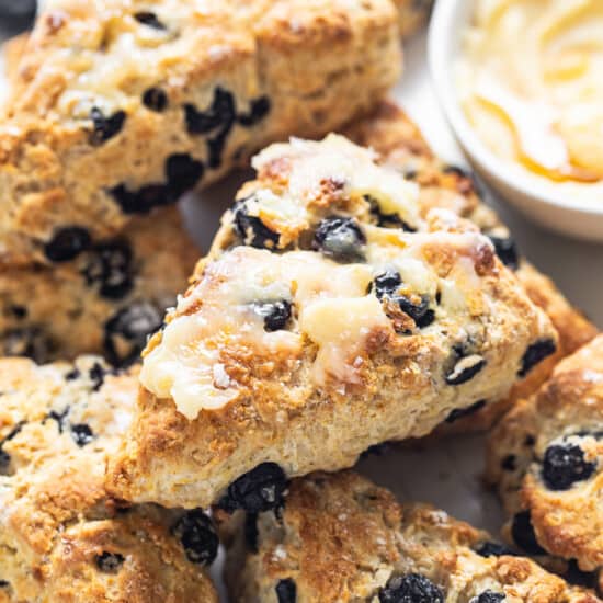 a white plate topped with blueberry scones next to a bowl of dip.
