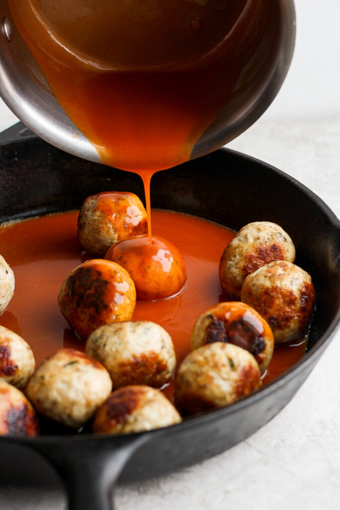 pouring buffalo sauce on top of meatballs.