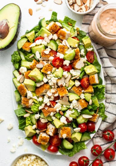 A salad with chicken, avocado, tomatoes and dressing on a white plate.