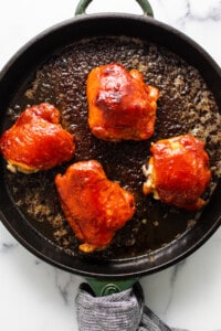 four pieces of chicken in a skillet on a marble counter top.