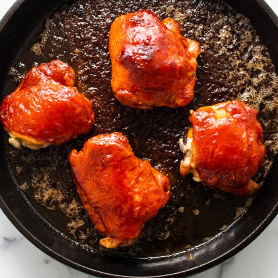 four pieces of chicken in a skillet on a marble counter top.