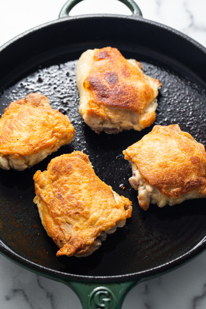 chicken thighs searing in a skillet.