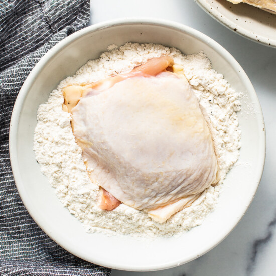 a white bowl filled with flour next to a chicken breast.