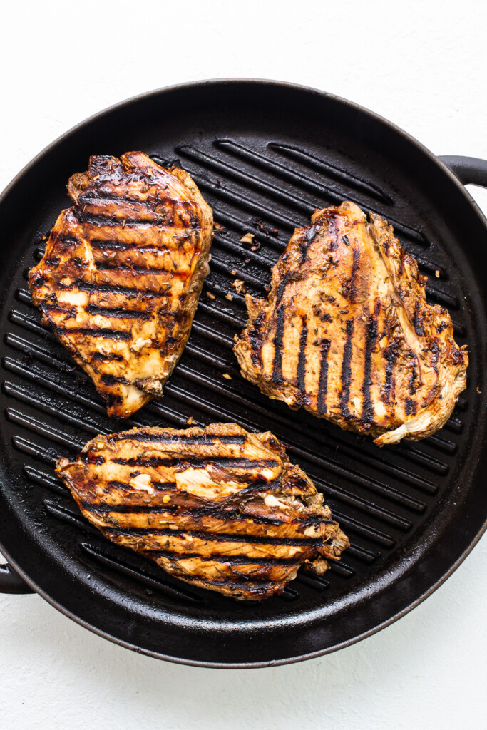 Grilled chicken breasts in a skillet on a white background.