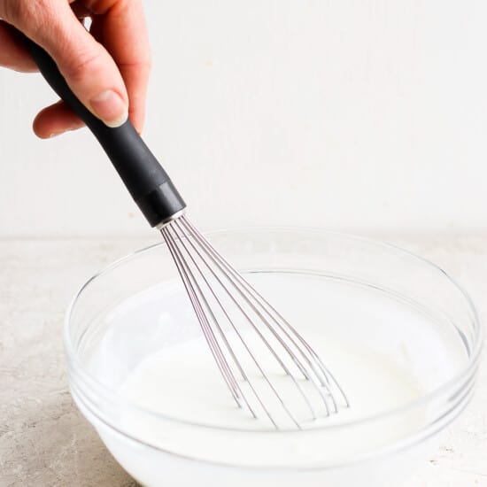 A person whisking milk in a glass bowl.