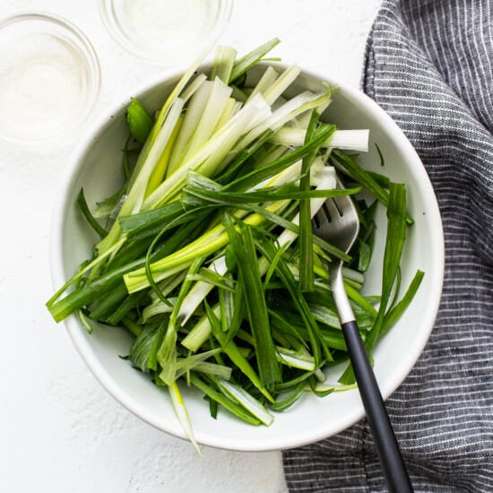 A white bowl with green onions and a fork.