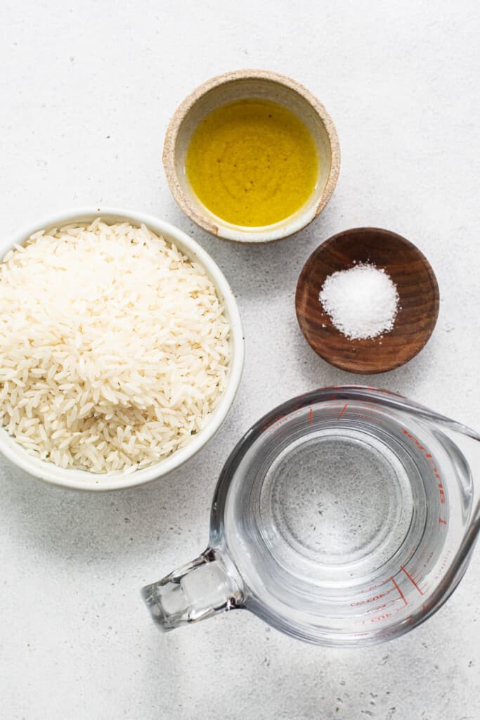 A bowl of rice, olive oil and salt on a white surface.