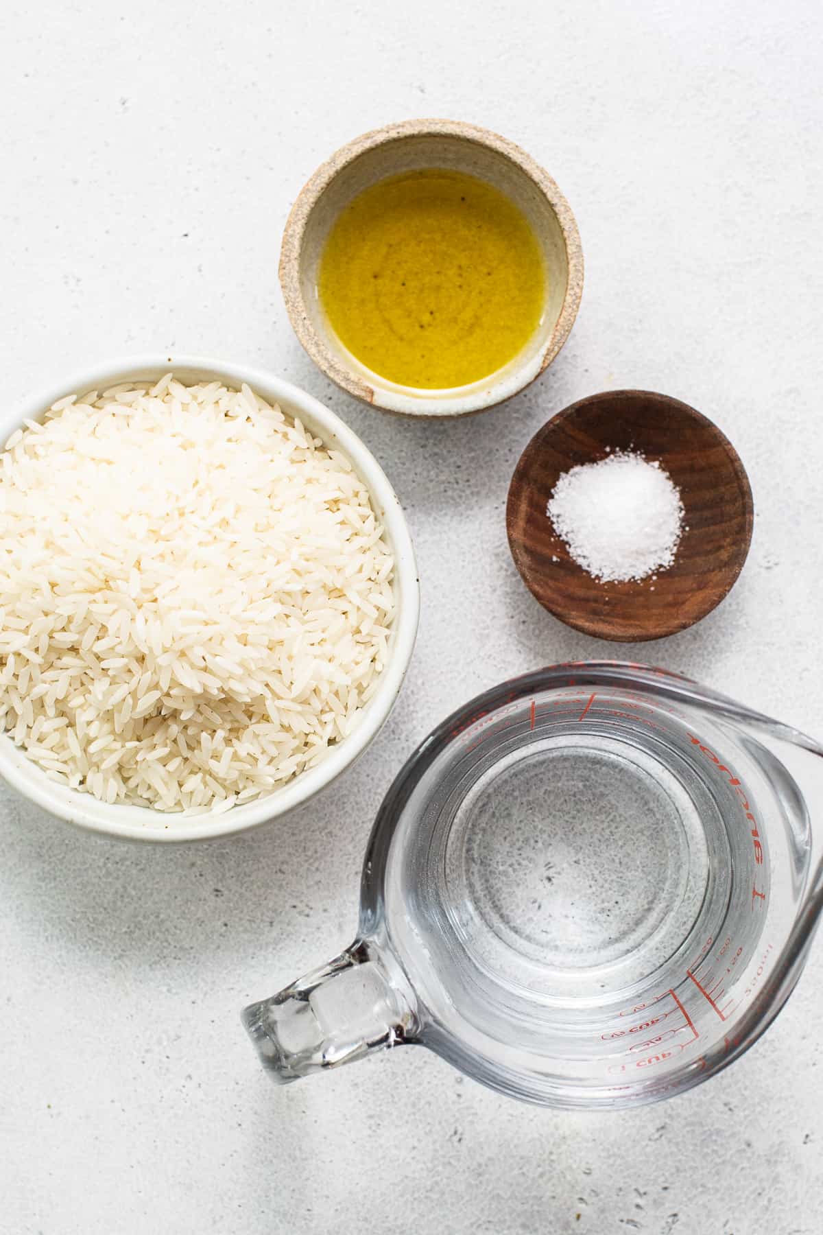 A bowl of rice, olive oil and salt on a white surface.