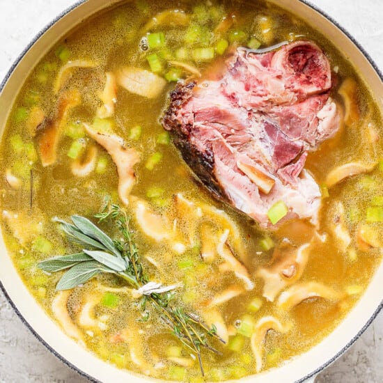 A pot of soup with meat, peas and sprigs of rosemary.