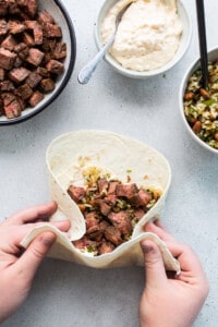 A person holding a burrito filled with beef and vegetables.