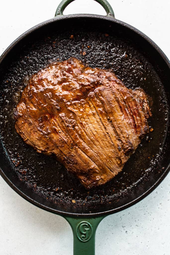 Flank steak seared in a cast iron pan.