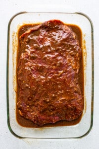 A glass baking dish with meat in a sauce.