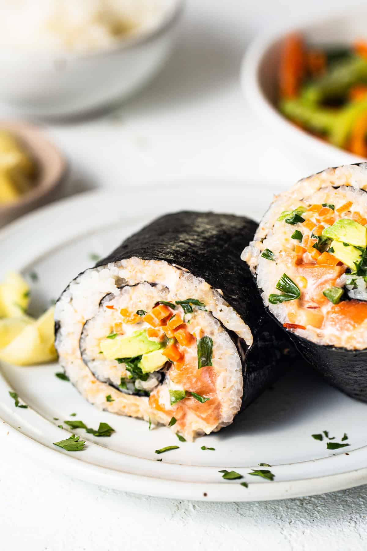 a white plate topped with sushi next to a bowl of vegetables.