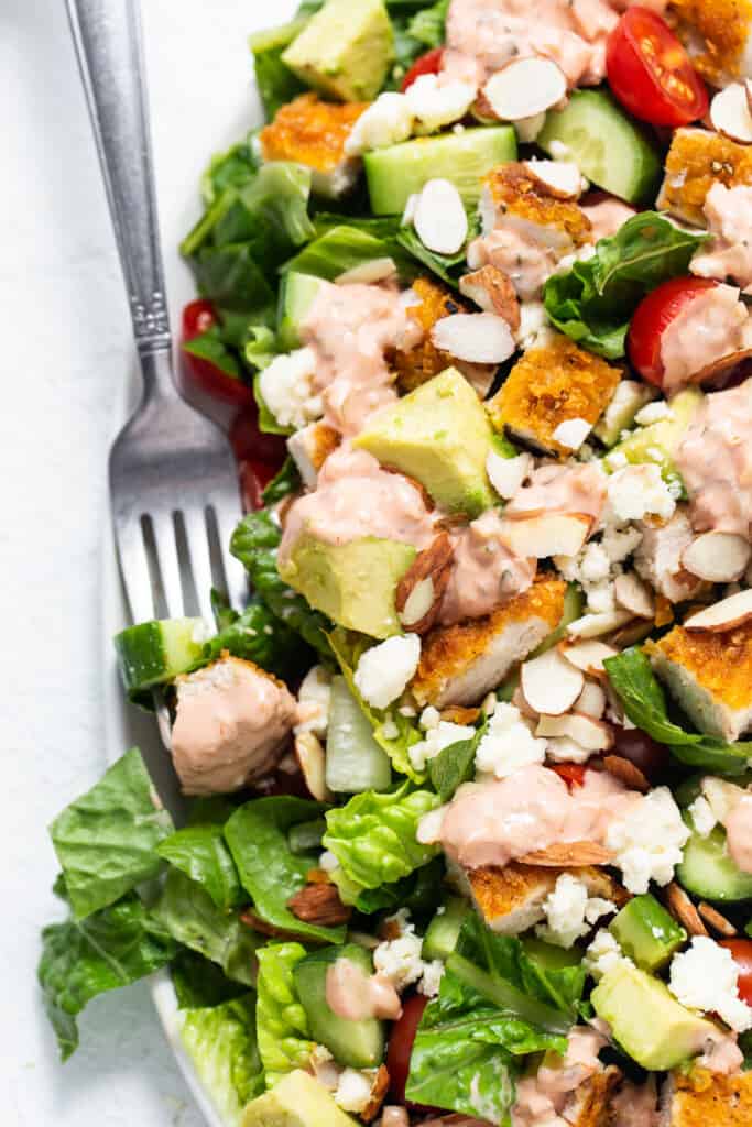 A salad with chicken, tomatoes, and avocado on a plate.