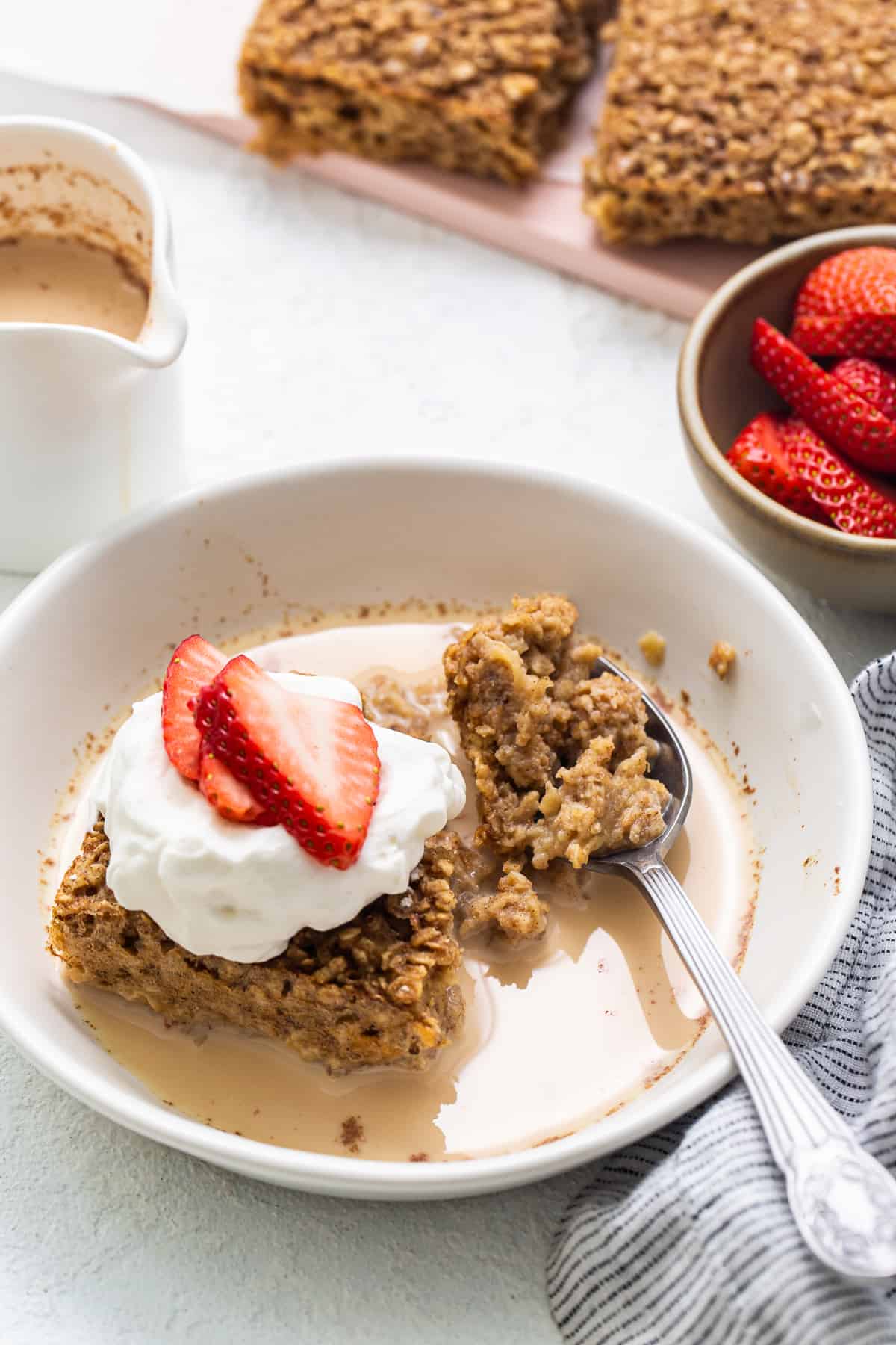 Slice of tres leches baked oatmeal topped with whipped cream and strawberries.