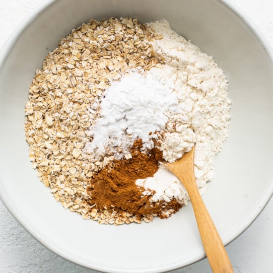 Oats and cinnamon in a bowl with a wooden spoon.