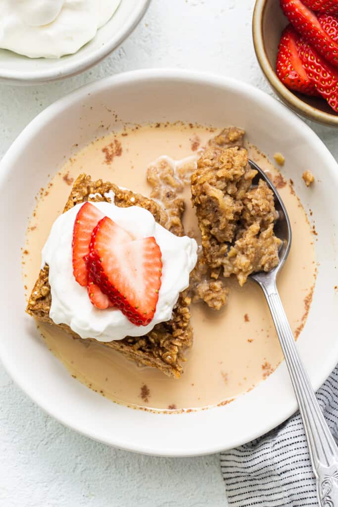 Slice of tres leches baked oatmeal in a bowl topped with strawberries.