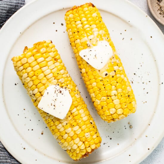 two corn on the cob with butter on top.