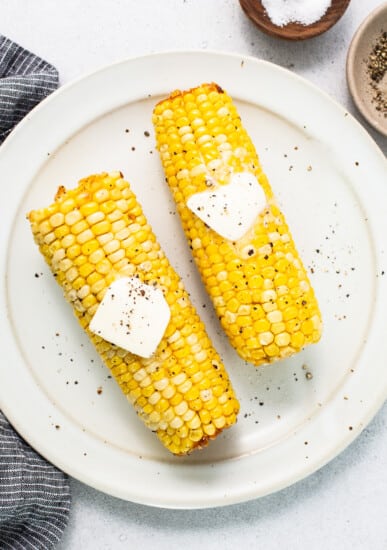 two corn on the cob with butter on top.