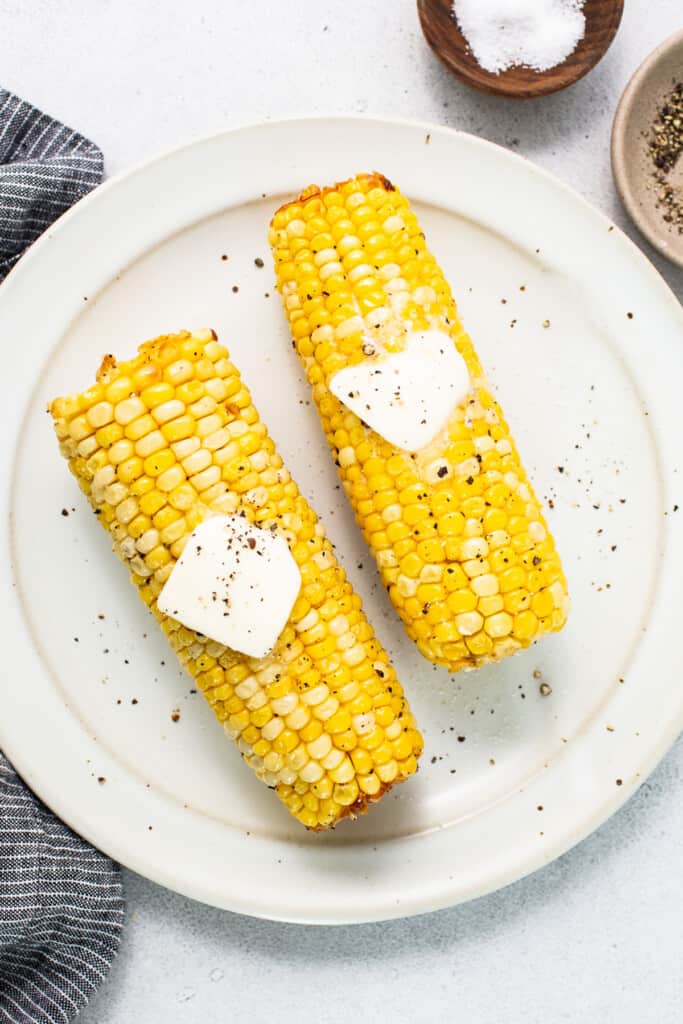 two corn on the cob with butter on top.