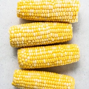 three ears of corn on a white surface.