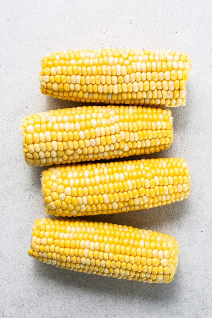 three ears of corn on a white surface.