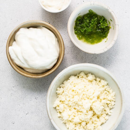 Three bowls of cheese, yogurt, and chives on a white surface.