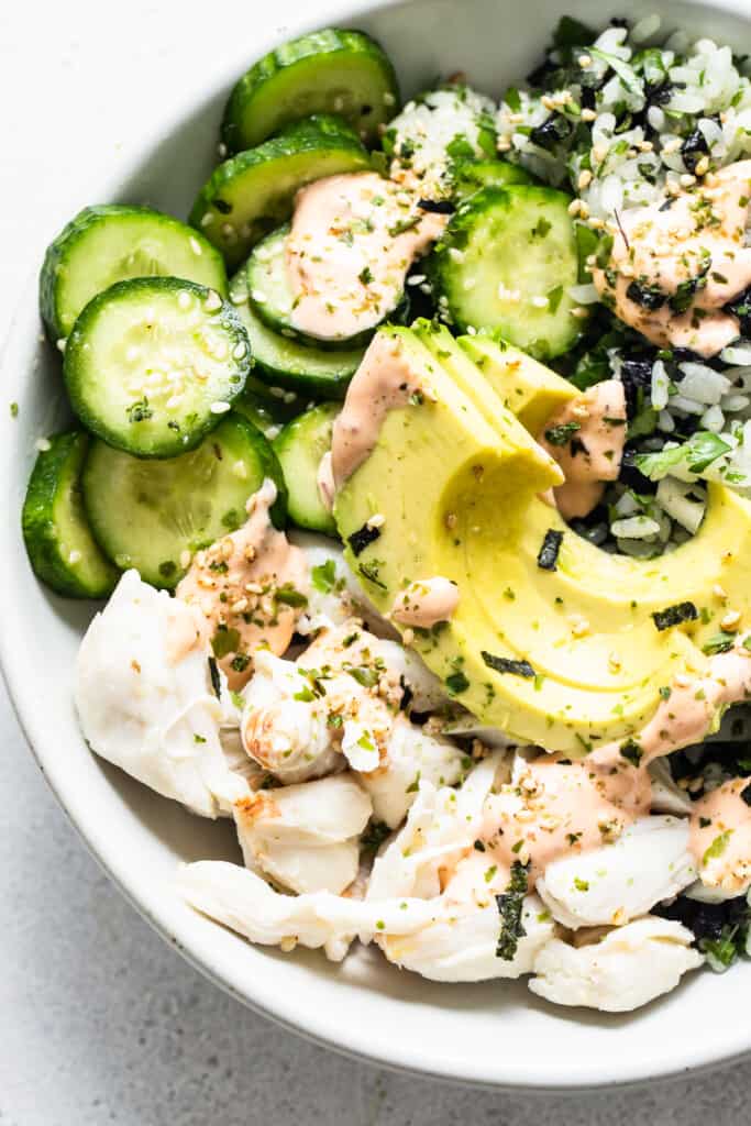 A bowl of sushi with cucumbers and avocado.