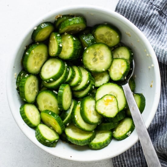 Cucumbers in a white bowl with a spoon.