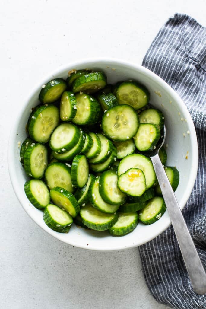 Cucumbers in a white bowl with a spoon.