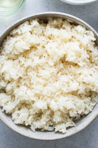 Rice in a bowl next to a bowl of water.