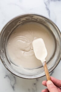 a hand holding a wooden spoon over a bowl of cream.