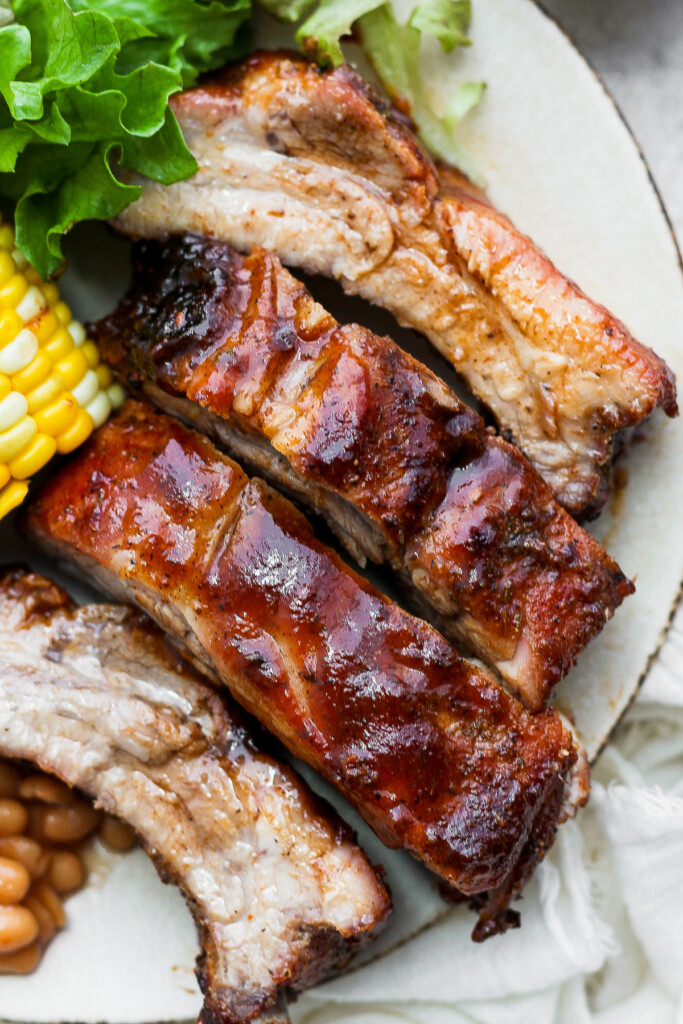 a white plate with ribs, corn and salad.