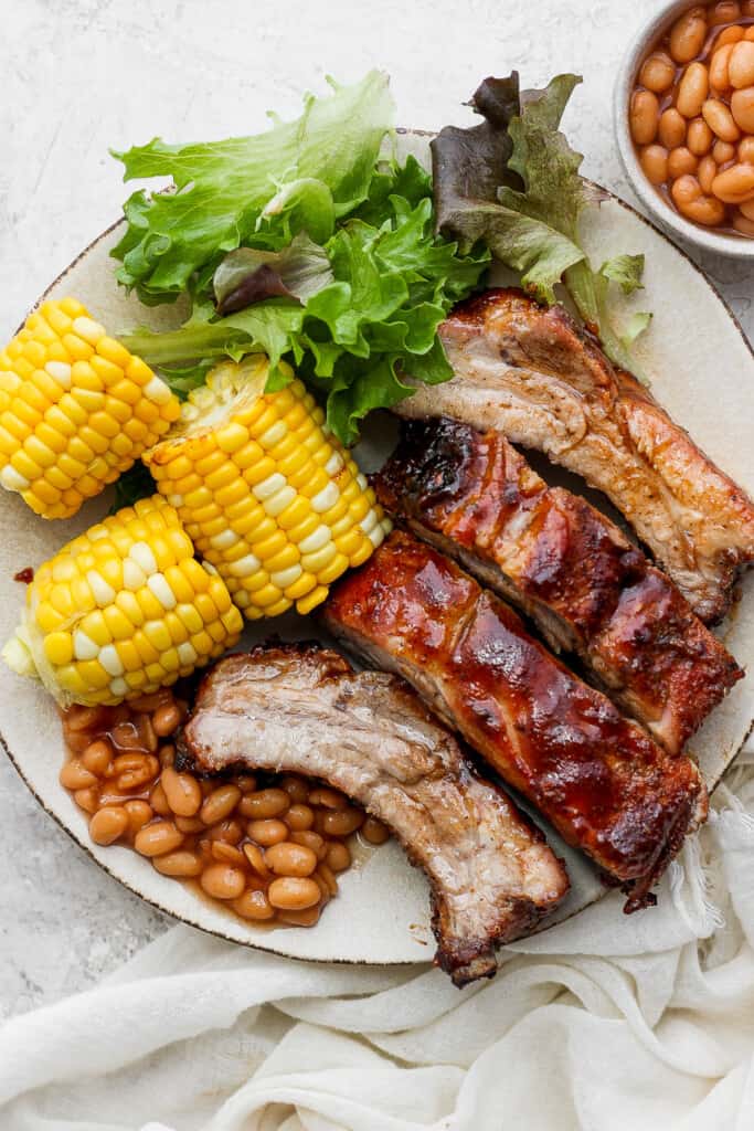 a plate with ribs, corn, beans, and lettuce.