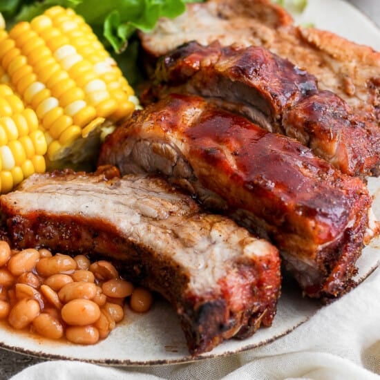 a plate of meat, beans, corn and corn on the cob.