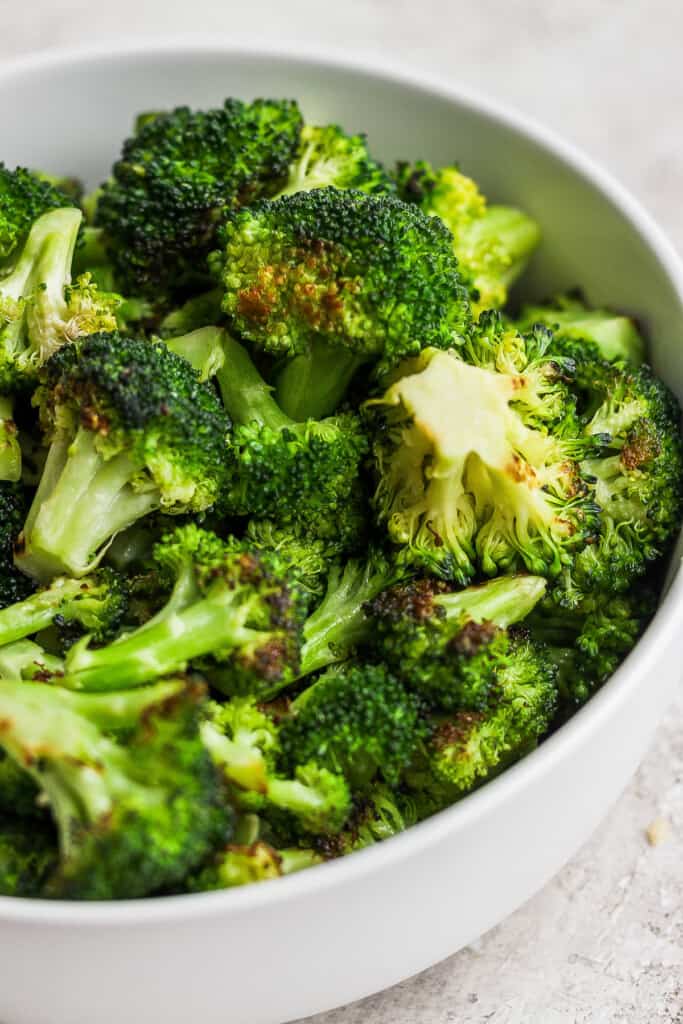 a white bowl filled with broccoli on top of a table.