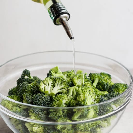 a bowl of broccoli and a bottle of olive oil.