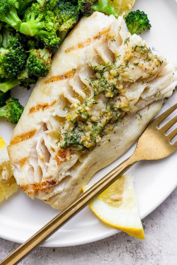 Grilled fish on a plate with broccoli.