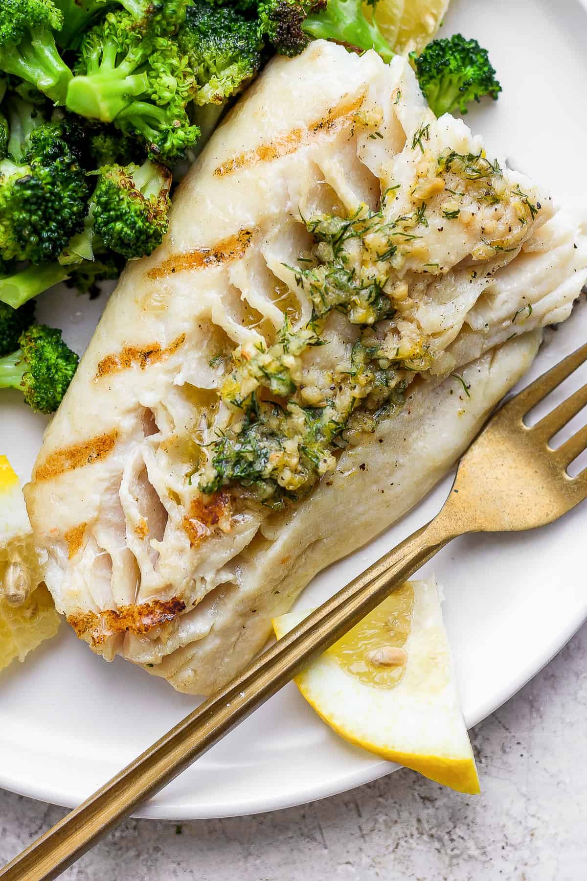 Grilled fish on a plate with broccoli.