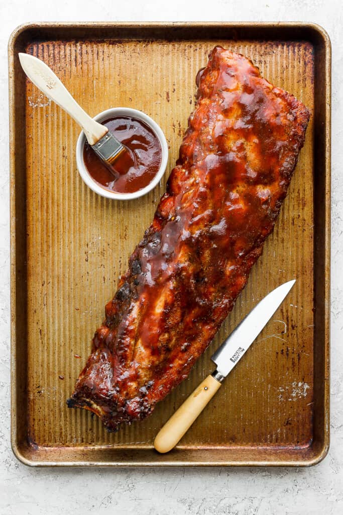 a bbq ribs on a tray with ketchup and a knife.