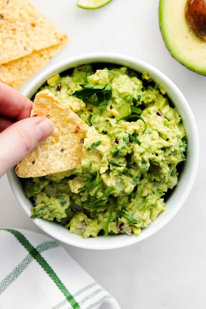guacamole in bowl with hand dipping.