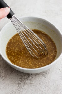 a hand holding a whisk in a bowl of brown liquid.