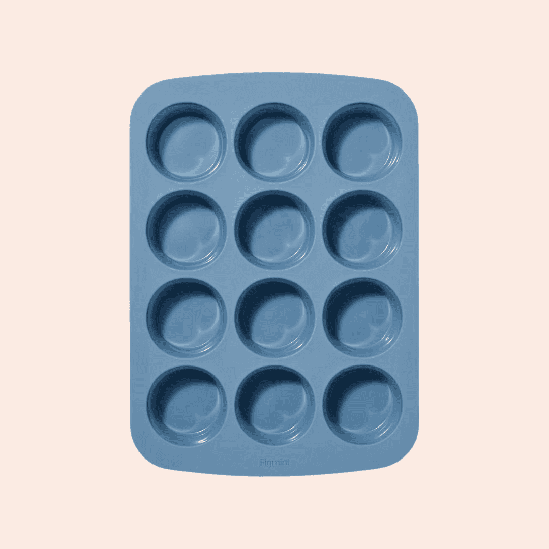 A blue silicone muffin tray with twelve round molds arranged in a three-by-four grid against a light background.