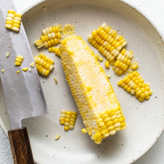 Corn on the cob on a plate with a knife.