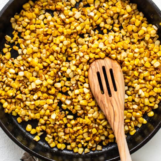corn in a skillet with a wooden spoon.