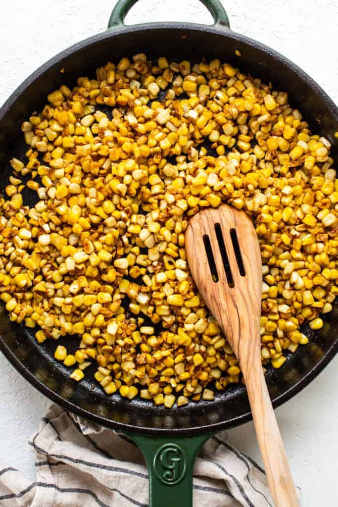 corn in a skillet with a wooden spoon.