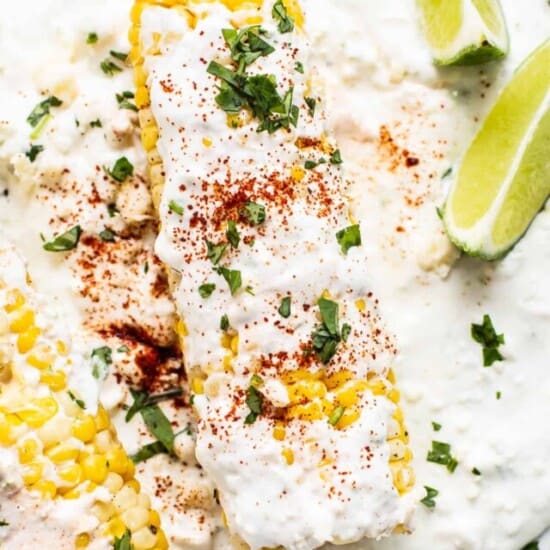 Air fryer elote on a plate with slices of lime.